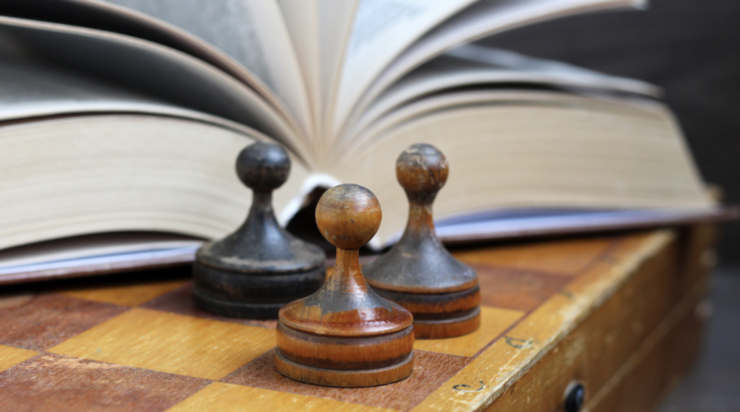 Three chess pawns next to an open book.