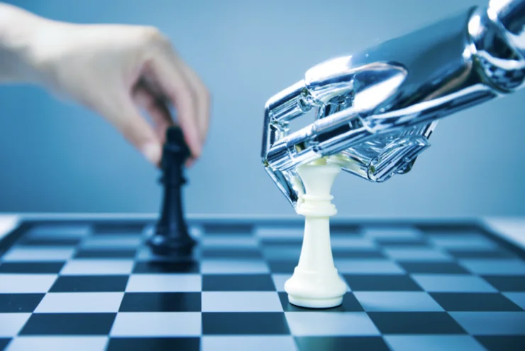 A human hand moving a black chess piece vs a robot hand moving a white chess piece.