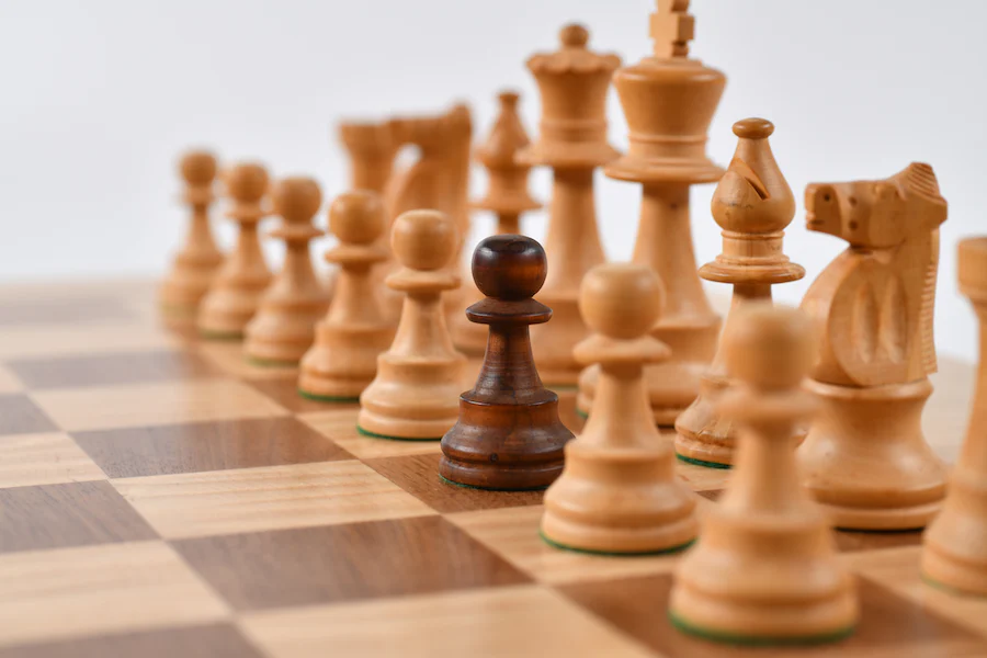 A black pawn in the middle of white chess pieces.