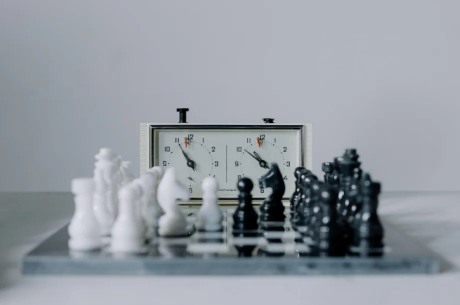 An analog chess clock next to a chess set.