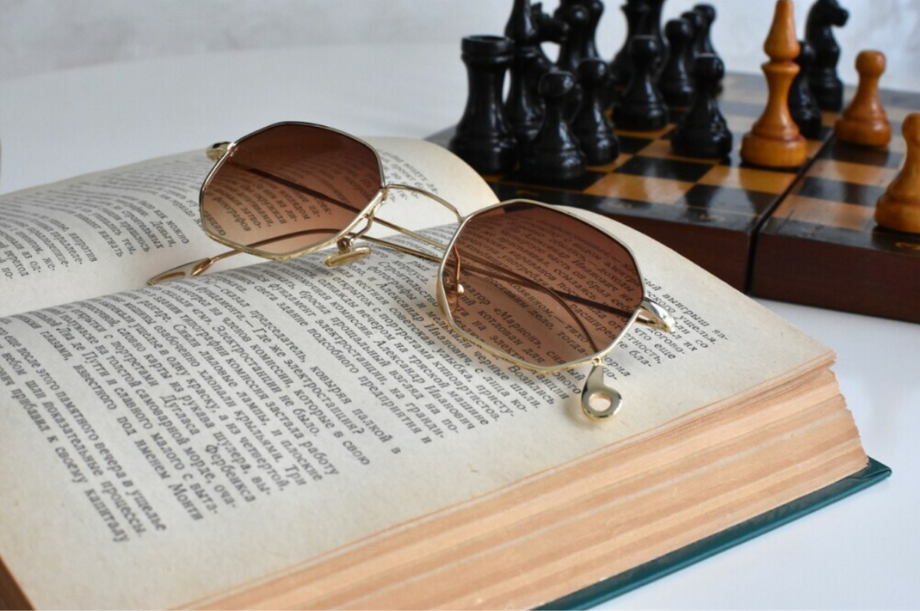 Sunglasses on top of a book placed next to a chess set.